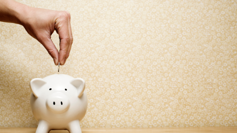 A hand putting money into a piggy bank.