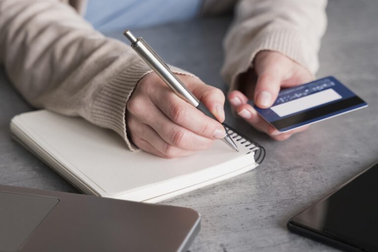 Person with credit card in hand making notes in notebook